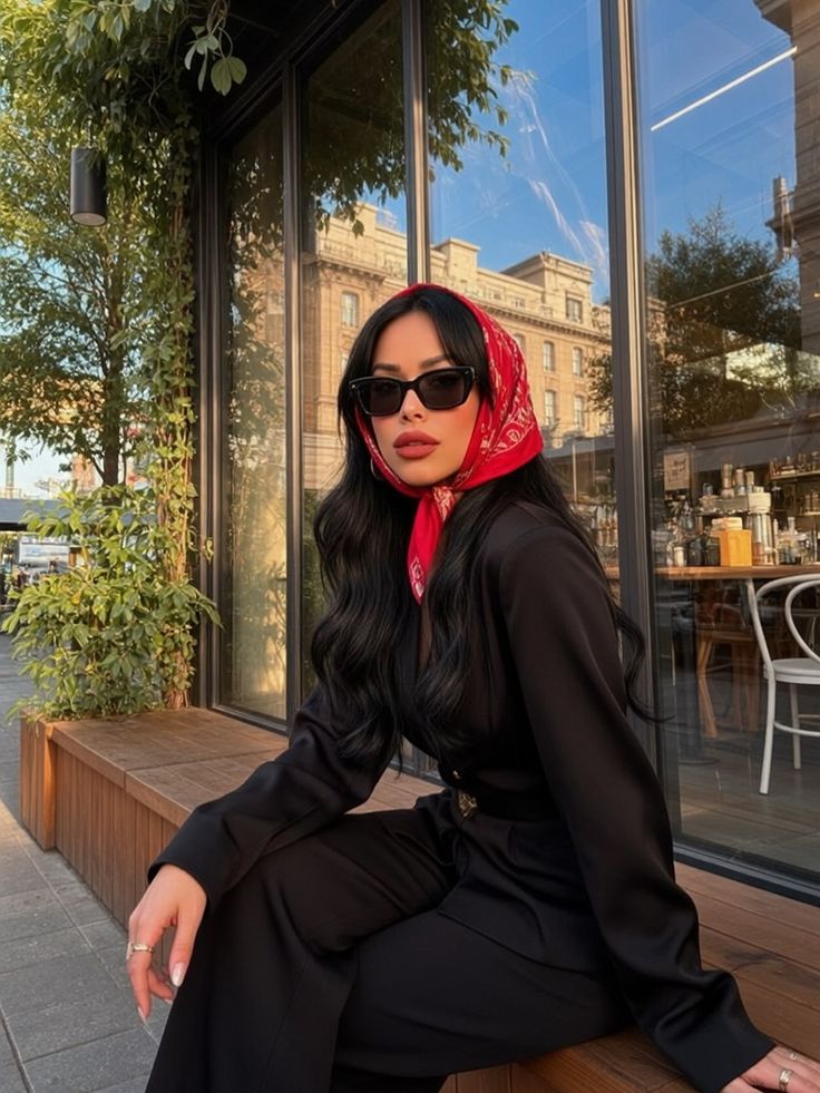 Model sitting wearing black jumpsuit with red bandana scarf
