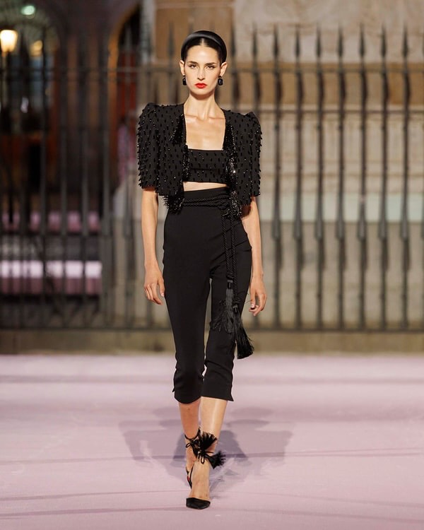 The Carolina Herrera Spring/Summer 2026 collection debuted on the runway with a monochrome look that includes an embellished cropped jacket, a bandeau tube top bra, and cropped skinny slacks