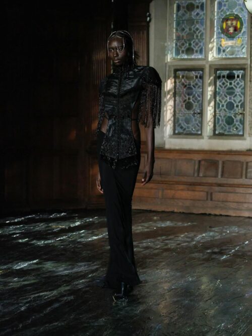 Dilara Findikoglu’s Spring 2026 collection included model Nyagua Ruea in a black cutout gown with a dramatic cape fringe top and sheer maxi, which Jenna Ortega also wore to the Golden Globes.