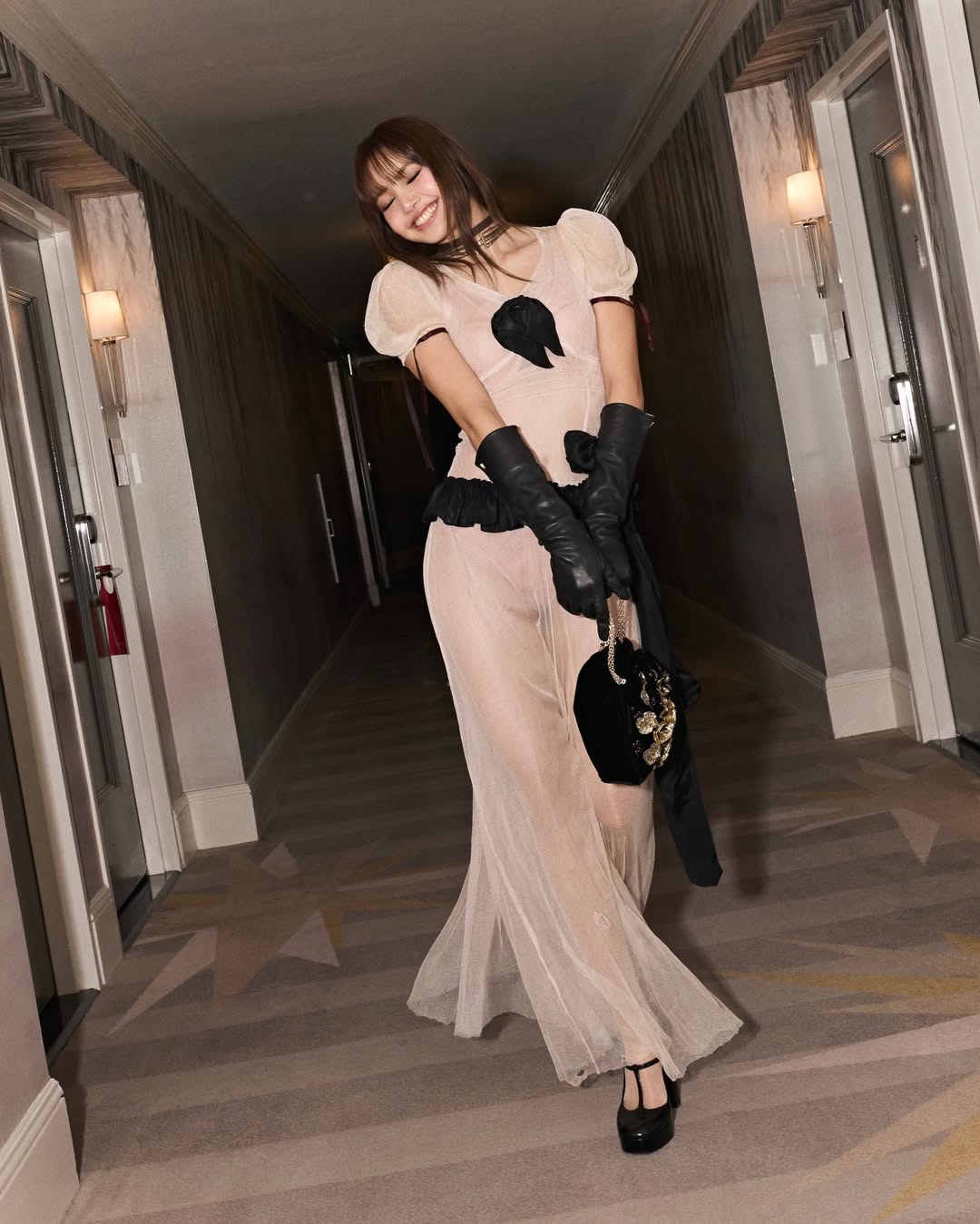 Blackpink Lisa attends the 2026 Golden Globes after-party dressed in an Enfants Riches Déprimés (ERD) Spring/Summer 2026 runway-inspired two-tone cream and white sheer maxi dress with a black bow tie, matching ruffled peplum waistline, and an extended black sash tied at the left hip and extending down the side of the dress.
