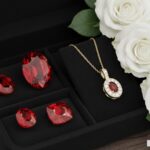 Some loose rubies and a ruby pendant in a black box. Add white roses at the side