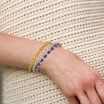 a woman layering a diamond bracelet with color gemstone bracelets