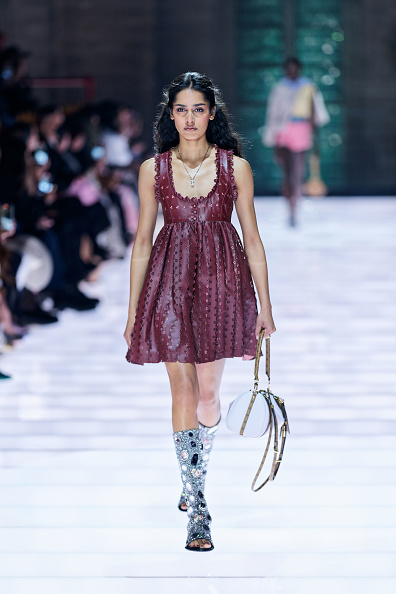 A model walks the runway wearing a burgundy short dress inspired by the Louis Vuitton Cruise 2026 collection.