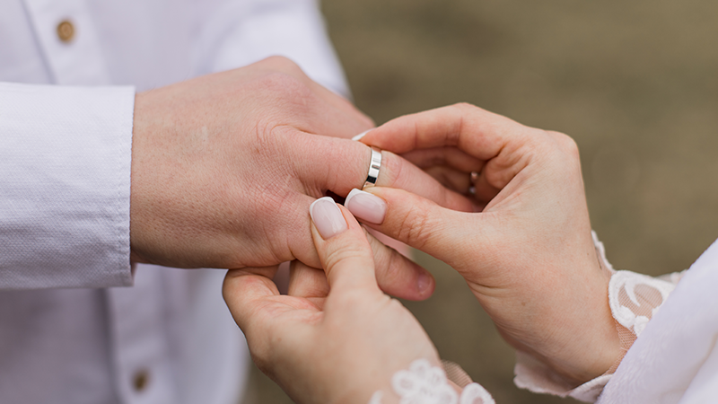 female hands placing wedding band on mans hand