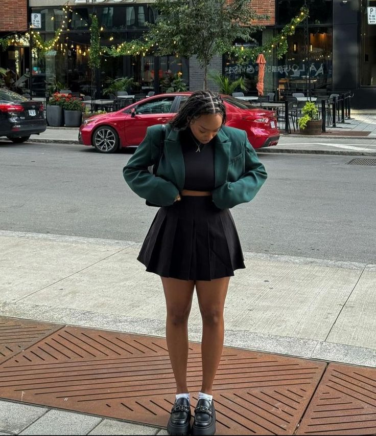 model in green blazer and black pleated mini skirt 