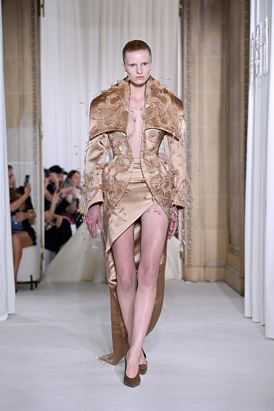 The Ashi Studio Haute Couture Fall/Winter 2025/2026 collection featured a long-sleeve satin coat with a wide shawl collar worn over a matching satin asymmetrical draped dress with a front thigh-high slit and a long train.