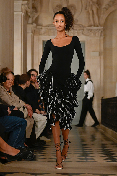 Mona Tougaard, a Danish fashion model, walks down the runway for Jacquemus’ Fall/Winter 2026 “Le Palmier” collection, wearing a long-sleeved scoop-neck midi dress with black and white frills.