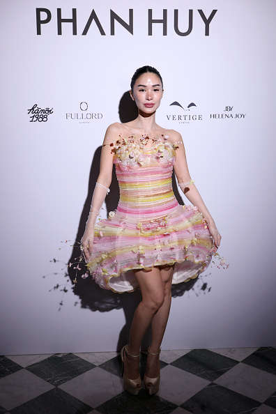 On the fourth day of Paris Fashion Week, Heart Evangelista wore a strapless bubble dress made of sheer white tulle with horizontal bands in pink, yellow, and white, adorned with three-dimensional floral appliqués and trailing vines.