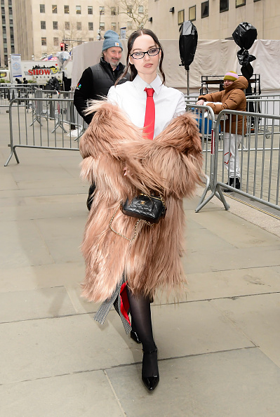 During the “56 Days” premiere promotional tour in New York, Dove Cameron wore a beige Ferrari fur coat, a black Chanel caviar leather mini Vanity bag, sheer pantyhose, and Andrea Wazen Demi black patent leather shoes.