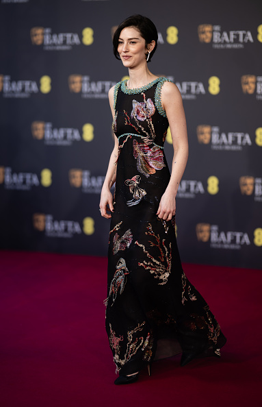 Gracie Abrams wore a Chanel embroidered maxi dress from the Métiers d’Art 2026 collection, patent leather pumps, and Chanel Coco Crush Transformable hoop drop earrings at the 2026 EE BAFTA Film Awards in London.