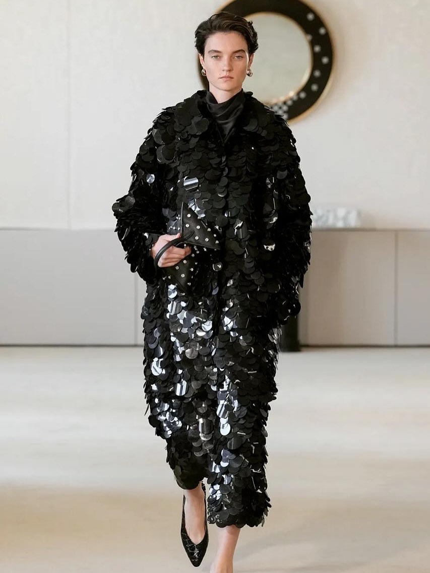 At the Altuzarra Spring/Summer 2026 show, a model elegantly presents a long black sequined coat as she strides along the runway.
