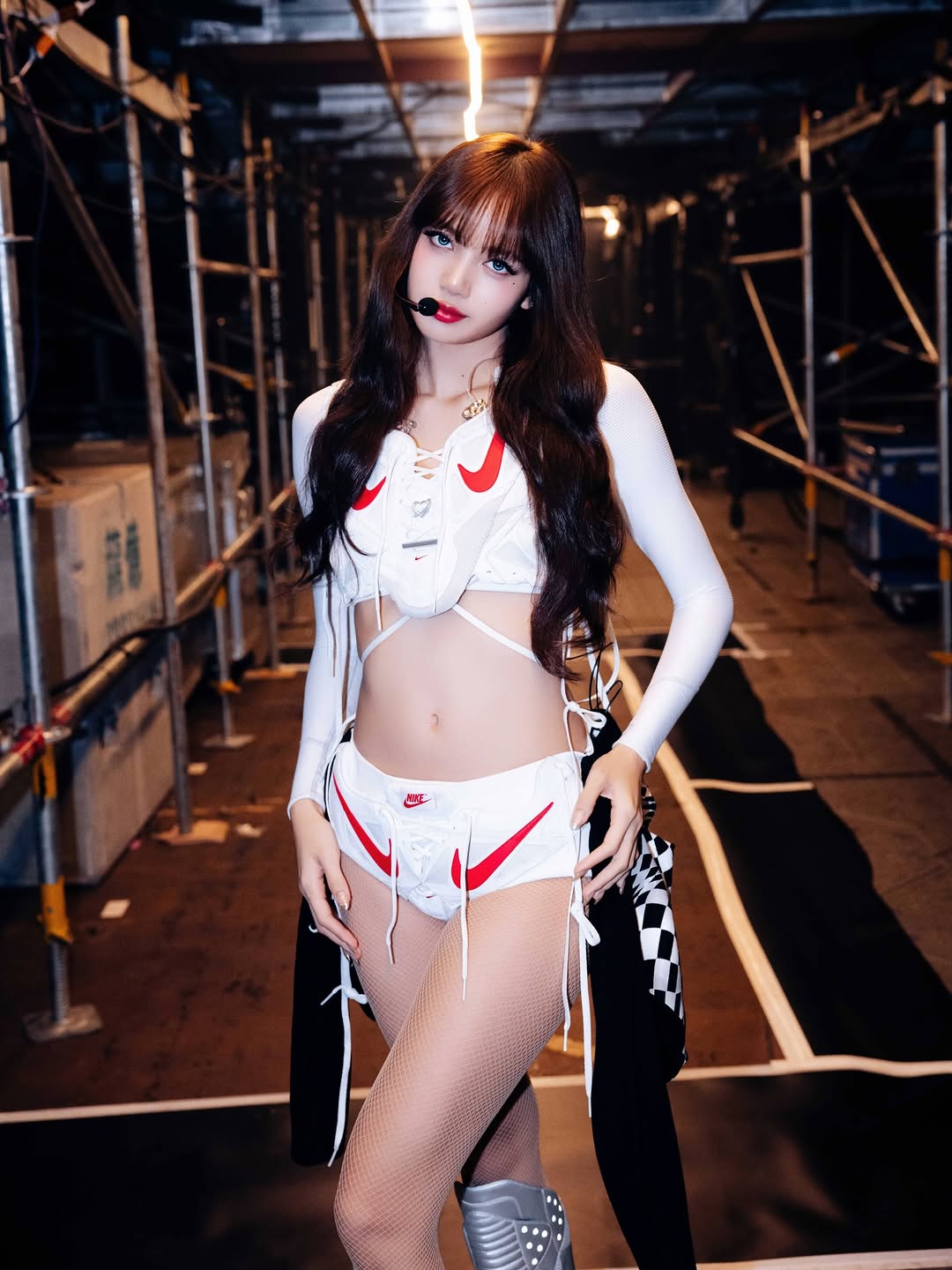 Blackpink Lisa wearing a long-sleeved lace-up corset embroidered with a bright red Nike logo and high-waisted shorts with eye-catching front lace-up elements.