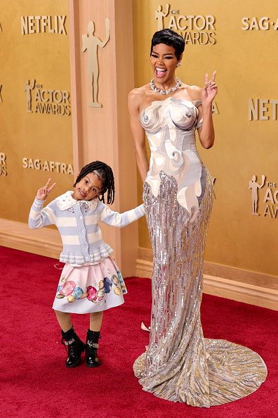 Teyana Taylor poses with her daughter Rue Rose Shumpert on the red carpet at the 2026 Actor Awards, dressed in a custom Thom Browne dress with a multicolored strapless top and sequin-beaded mermaid skirt, as well as Thom Browne nubuck platform saddle shoes.
