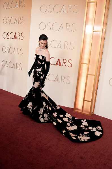 Anne Hathaway attended the 98th Academy Awards wearing a black Valentino Haute Couture velvet dress featuring hand-painted pink satin floral embroidery, retouched with gold tubes and silver center holes, and a mermaid sweeping train.