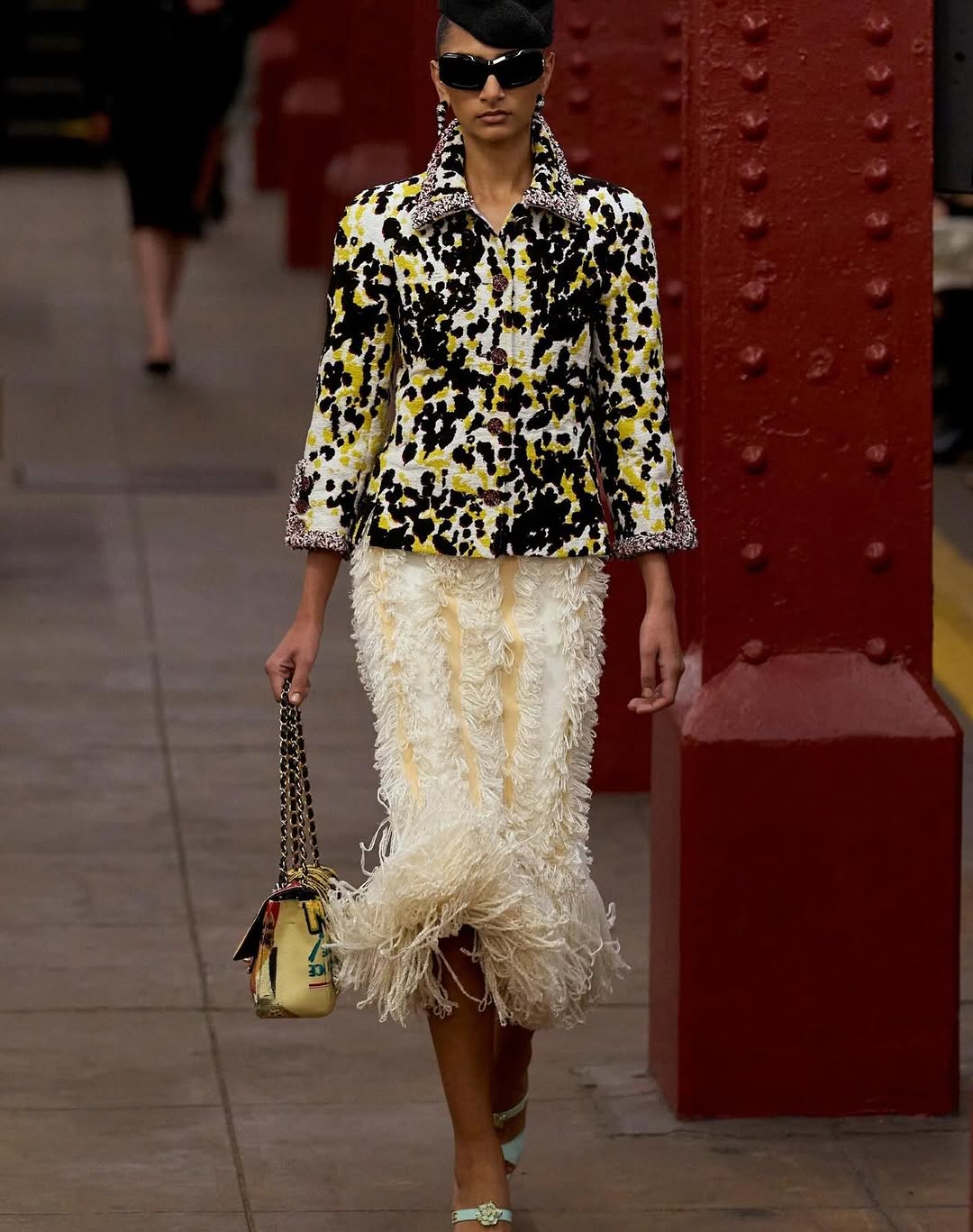 Maya Anand was spotted strolling through the Bowery subway station, modeling a multicolored tweed jacket paired with a knit fringe skirt for the Chanel Métiers d’Art 2026 ready-to-wear collection.