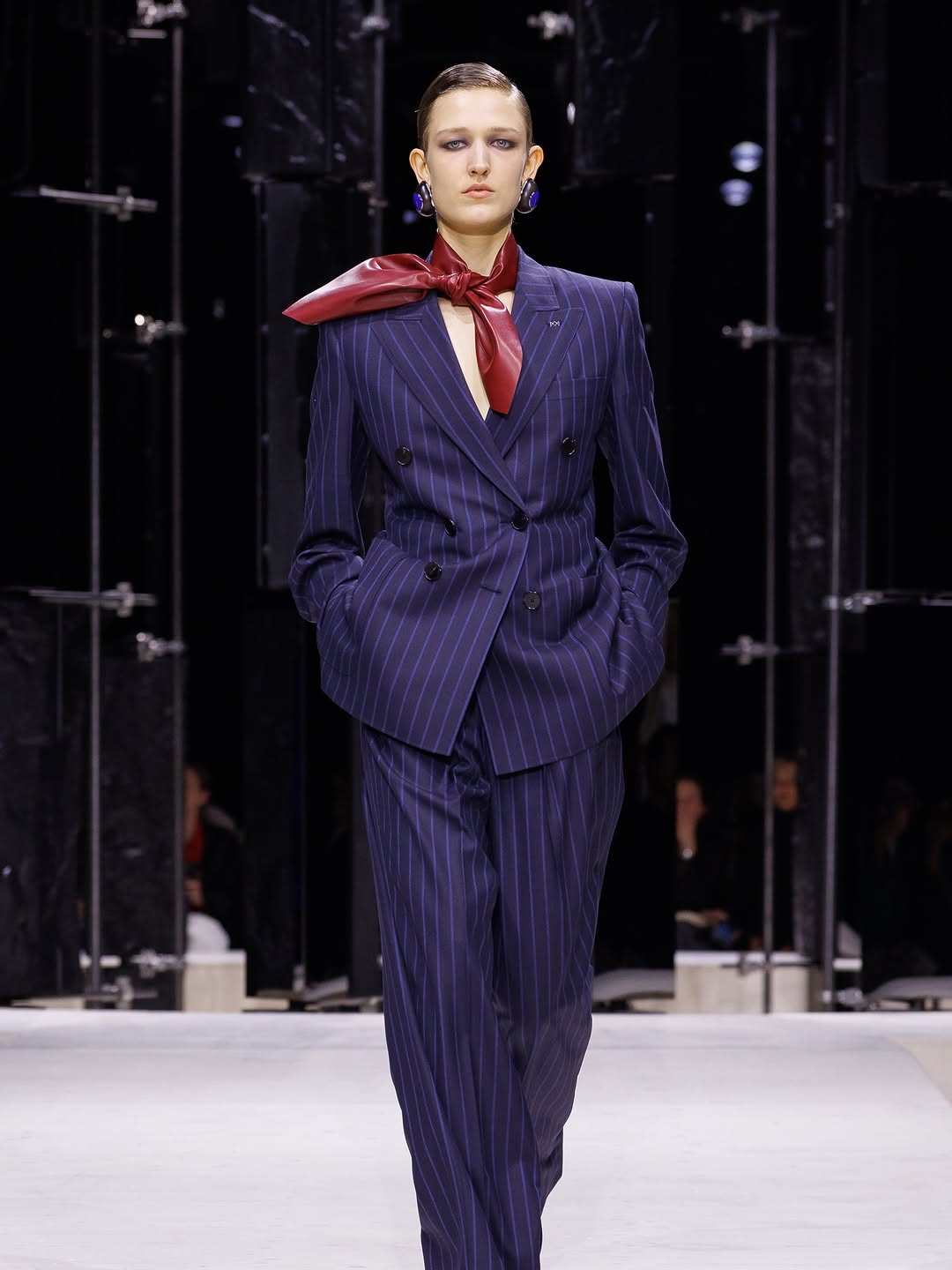 The Givenchy Ready-to-Wear collection for Fall/Winter 2026/2027 featured a navy blue wool double-breasted jacket with pinstripes, paired with matching double-pleated trousers, an oxblood leather neck scarf, and sculpted gem earrings.