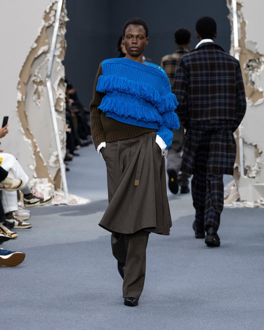 The Sacai Fall/Winter 2026 Menswear collection included a frilled knit pullover and a pleated midi skirt with wide-leg trousers underneath.