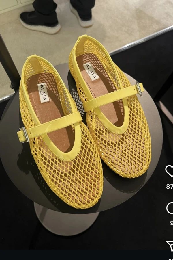 Pair of butter yellow mesh slip-on shoes with a buckle strap, displayed on a black round pedestal.