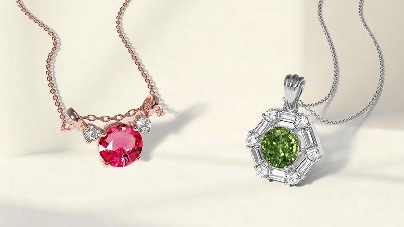 Two Sapphire necklaces on a light surface: one rose‑gold with a pink gem and diamond accents, the other silver with a green gem surrounded by diamonds.