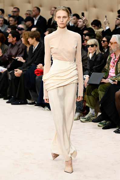 The Ferrari Fall/Winter 2026 “Skins I Am” collection included a beige turtleneck bodysuit combined with a high-waisted silk-satin maxi skirt with a side slit and draped asymmetrical ruched waist.