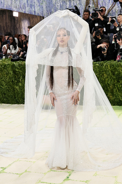 Blackpink Lisa presented a striking and impeccably tailored look at the 2026 Met Gala: Costume Art, wearing a custom Robert Wun couture ensemble featuring a sheer maxi veil supported by 3D-scanned arm structures from the shoulders, alongside a long-sleeved mock-neck Swarovski mermaid gown.