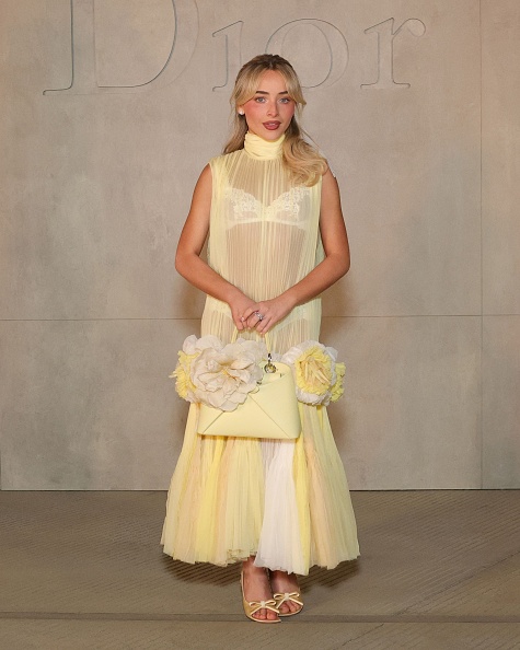 Sabrina Carpenter appeared at the 2027 Dior Cruise Collection Show dressed in a Christian Dior sheer pleated tulle gown, Dior bow slingback sandals, and a Dior “Cigale” bag.