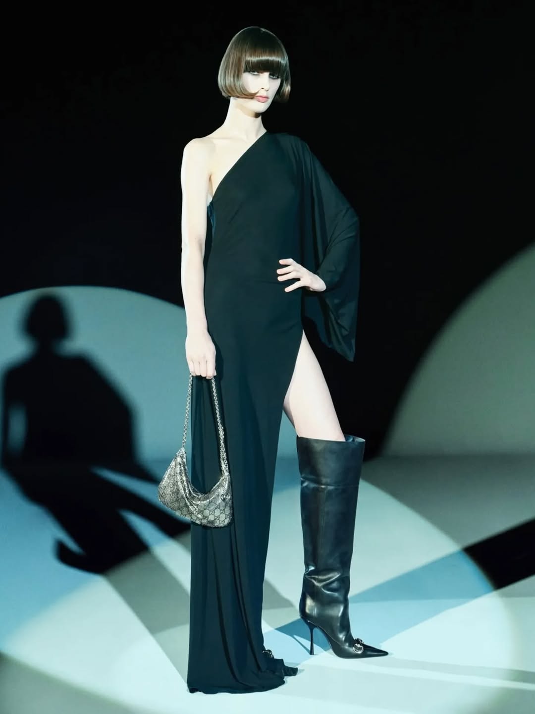Gucci’s Pre-Fall 2026 “Generation Gucci” collection featured a black one-shoulder gown with an asymmetrical neckline, a cape sleeve, and a thigh-high side split.