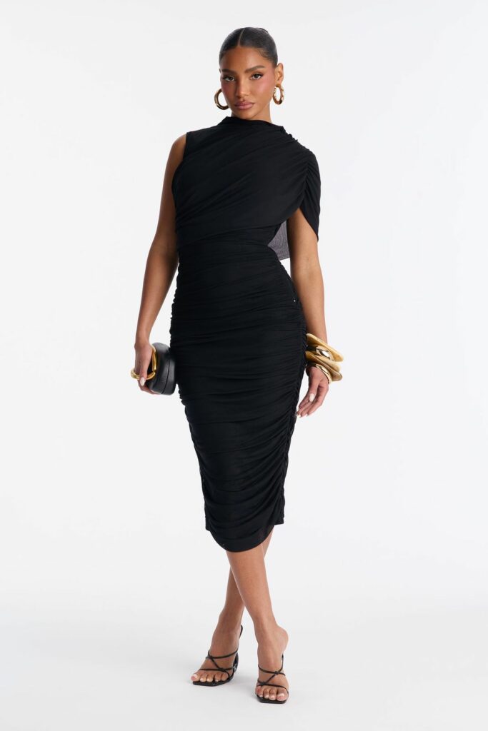 Model in a black ruched midi dress with a draped one-shoulder design, holding a black clutch with a gold handle and wearing gold hoops and bracelets.