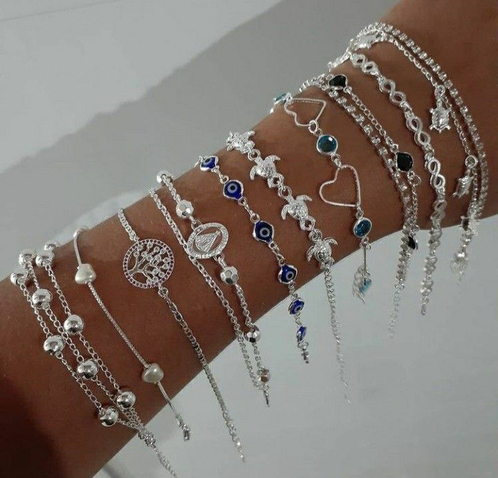 A collection of silver bracelets with various charms and beads worn on a forearm, including hearts, beads, and circular motifs.