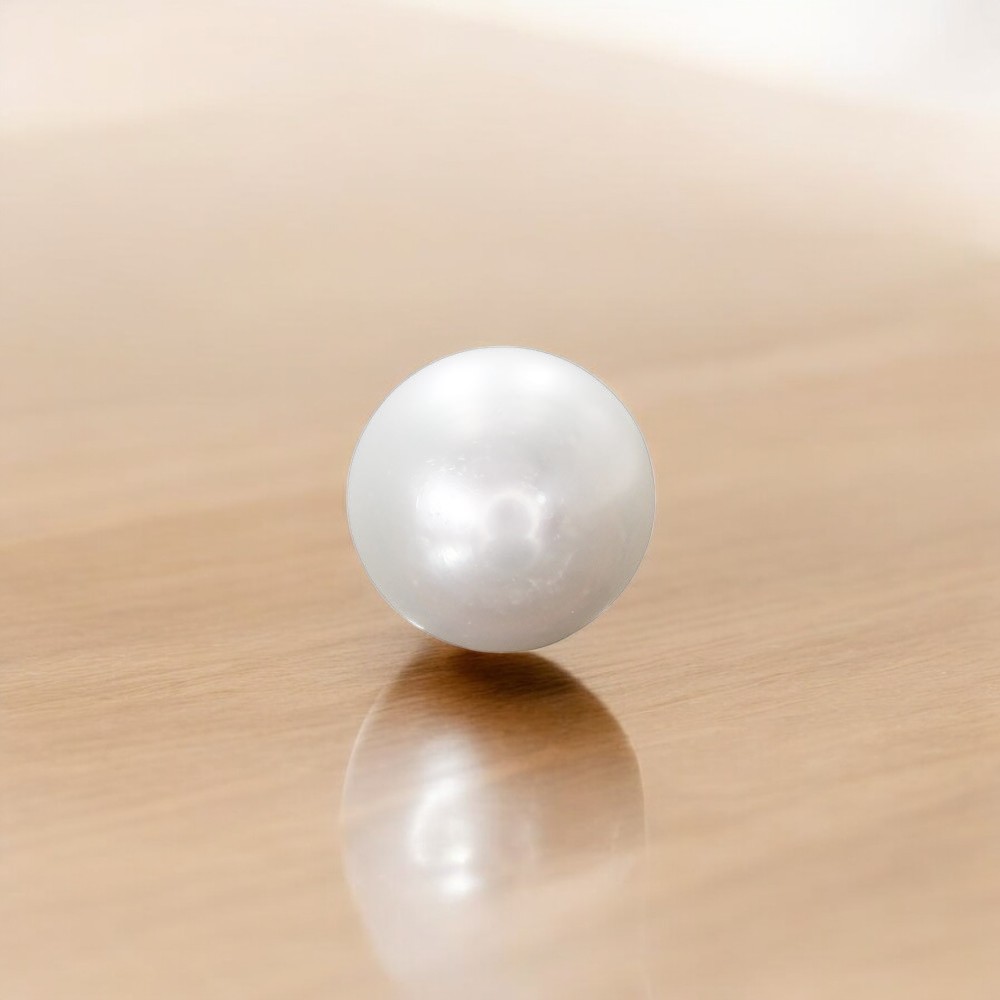Why June Has Three Birthstones - White pearl resting on a polished wooden surface with a soft reflection beneath it