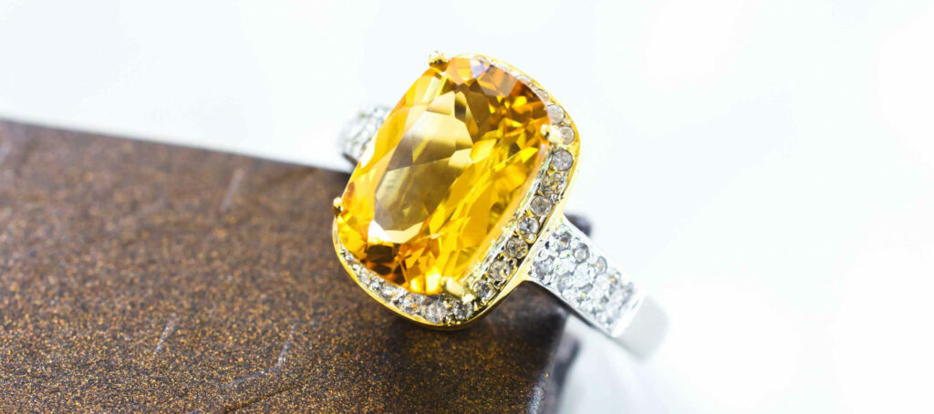Gold Yellow Sapphire Rings with a large yellow gemstone bordered by a halo of diamonds on a brown textured surface, close-up view