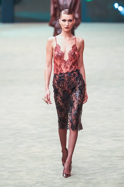 Bella Hadid walked the runway at Saint Laurent’s Women’s Fall/Winter 2026–2027 show wearing a sleeveless Chantilly lace bodysuit with a floral design, paired with a high-waisted sheer midi skirt.