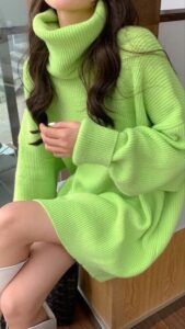 Person wearing a lime-green oversized turtleneck knit sweater seated indoors, with legs visible.