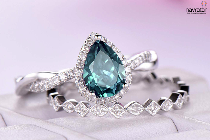 Teardrop teal gemstone ring with a diamond halo, displayed on a soft pink background alongside a diamond bracelet. Alexandrite Stone Pendant