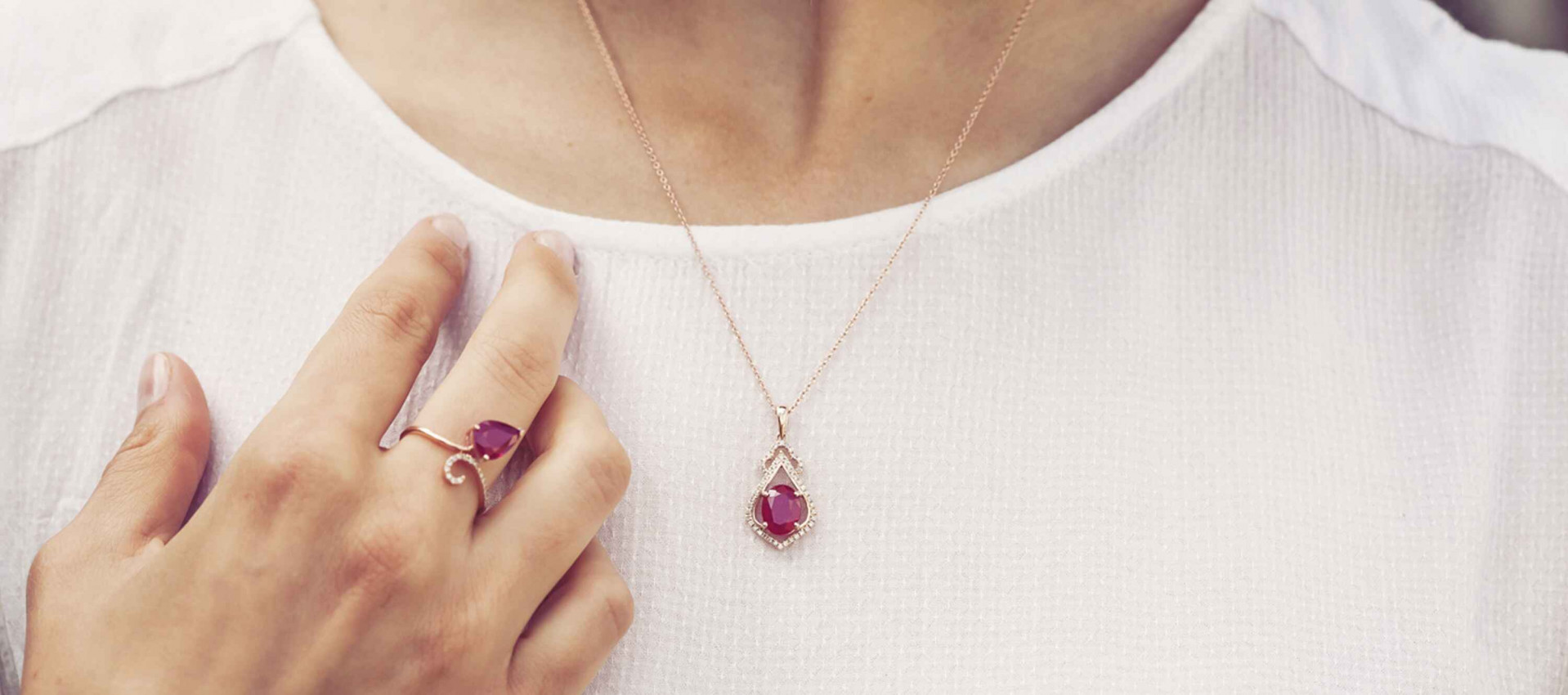 Rose gold teardrop pendant necklace with a manik stone, paired with a matching purple gem ring on a white textured top.