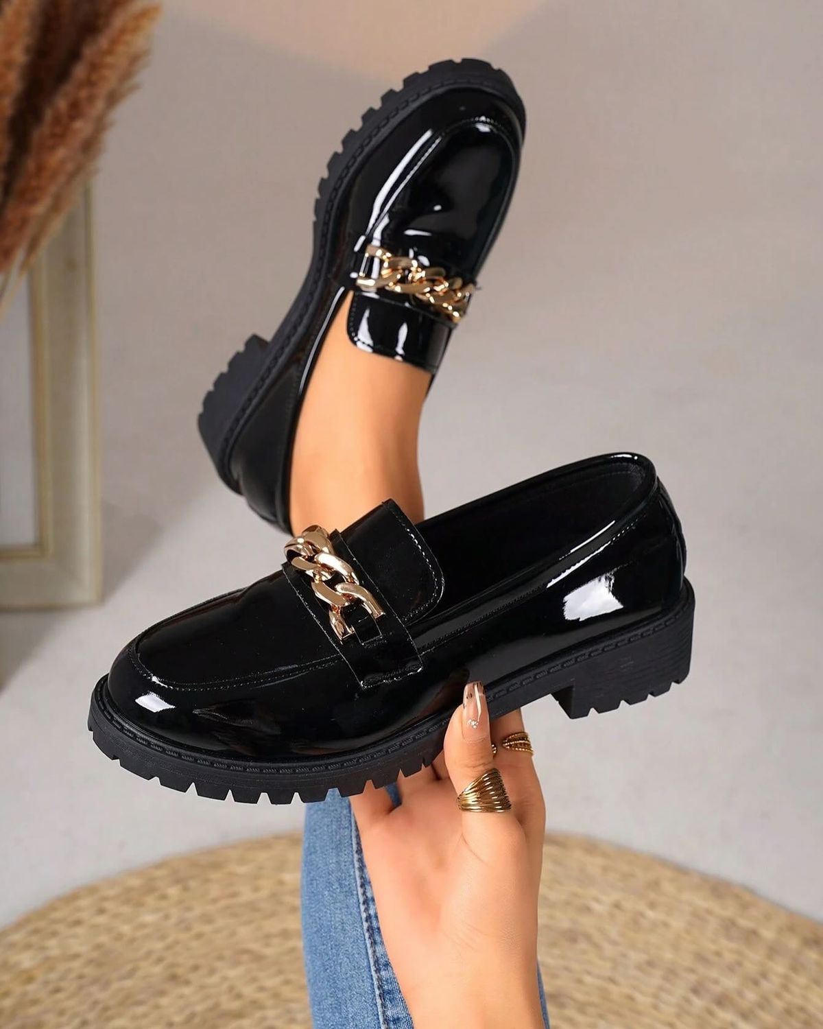 black patent leather loafers with a chunky lug sole and gold chain detail, shown as a fashion shoe.