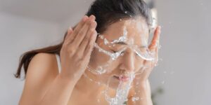 Woman washing her face with water splashing across her cheeks and eyes closed.