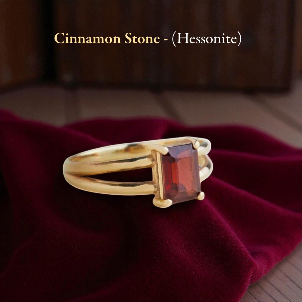 Gold ring featuring a rectangular red  Hessonite Stone in a four-prong setting resting on burgundy velvet fabric