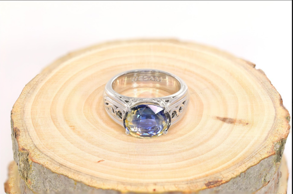 Silver ring with an Bi-Color Sapphire placed on a wooden log slice