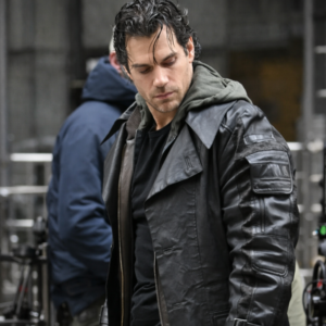 Man in a black leather jacket looking down, outdoors in an urban setting, with wet hair and a dark shirt underneath.