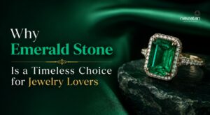 Emerald-cut ring with a diamond halo resting on a dark rock against a green backdrop, with headline about emerald stones.