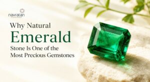 Emerald gemstone on a sandy surface with the headline 'Why Natural Emerald Stone Is One of the Most Precious Gemstones' and the Navratan logo