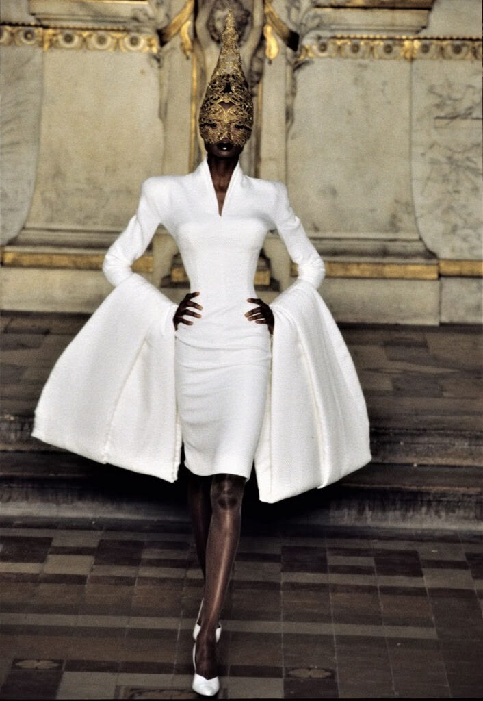 Debra Shaw walked the Givenchy Haute Couture Spring/Summer 1997 runway in a white knee-length dress with long sleeves and a Philip Treacy gold lace Eiffel Tower–inspired headdress.