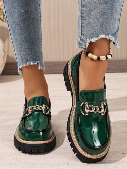 Pair of glossy emerald green patent loafers with a gold chain detail and chunky black sole, worn with frayed jeans.