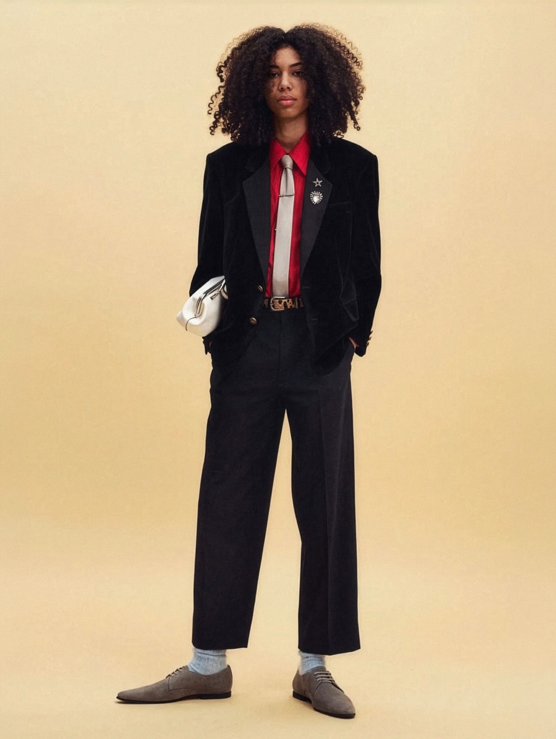 The Coach Resort 2027 line featured a tailored set: a black blazer jacket paired with a scarlet red long-sleeved silk button-up, styled with a light grey skinny tie, and finished with black high-waisted wide-leg pleated trousers—a styling worn by Zendaya during her “Spider-Man: Brand New Day” Shanghai premiere tour.