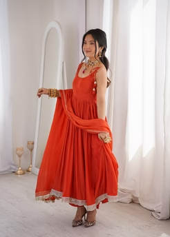 Full-length shot of a woman in a flowing red dress with white lace trim, standing in a bright, sunlit room near a mirror.