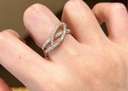 Close-up of a hand wearing a diamond-encrusted interlocking-loop engagement ring on the finger