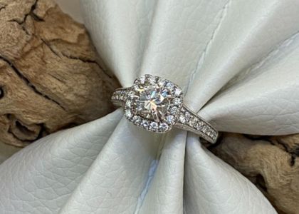 Diamond halo engagement ring resting on pale gray fabric with a wood background edge.