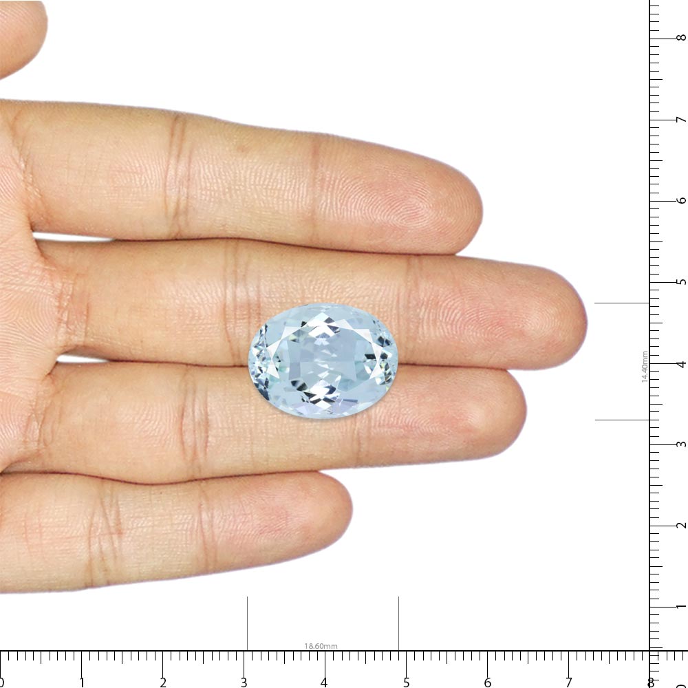 Oval light-blue gemstone held between a person's fingers with measurement rulers in the background, showing scale. aquamarine rings