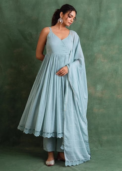 Woman modeling a light blue, ankle-length dress with a matching dupatta against a green backdrop, standing with hands at her waist.